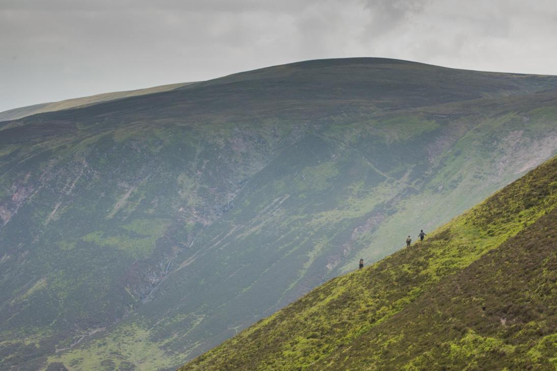 A landscape photo showing three small figures walking across a hill